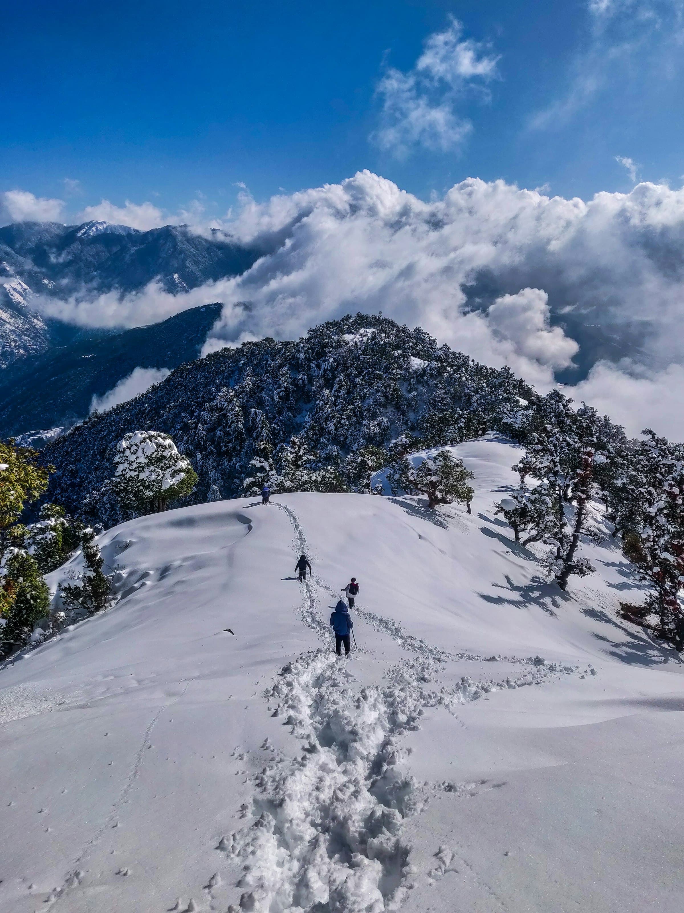 Trekkers descending a snowy ridge above cloud-filled valleys